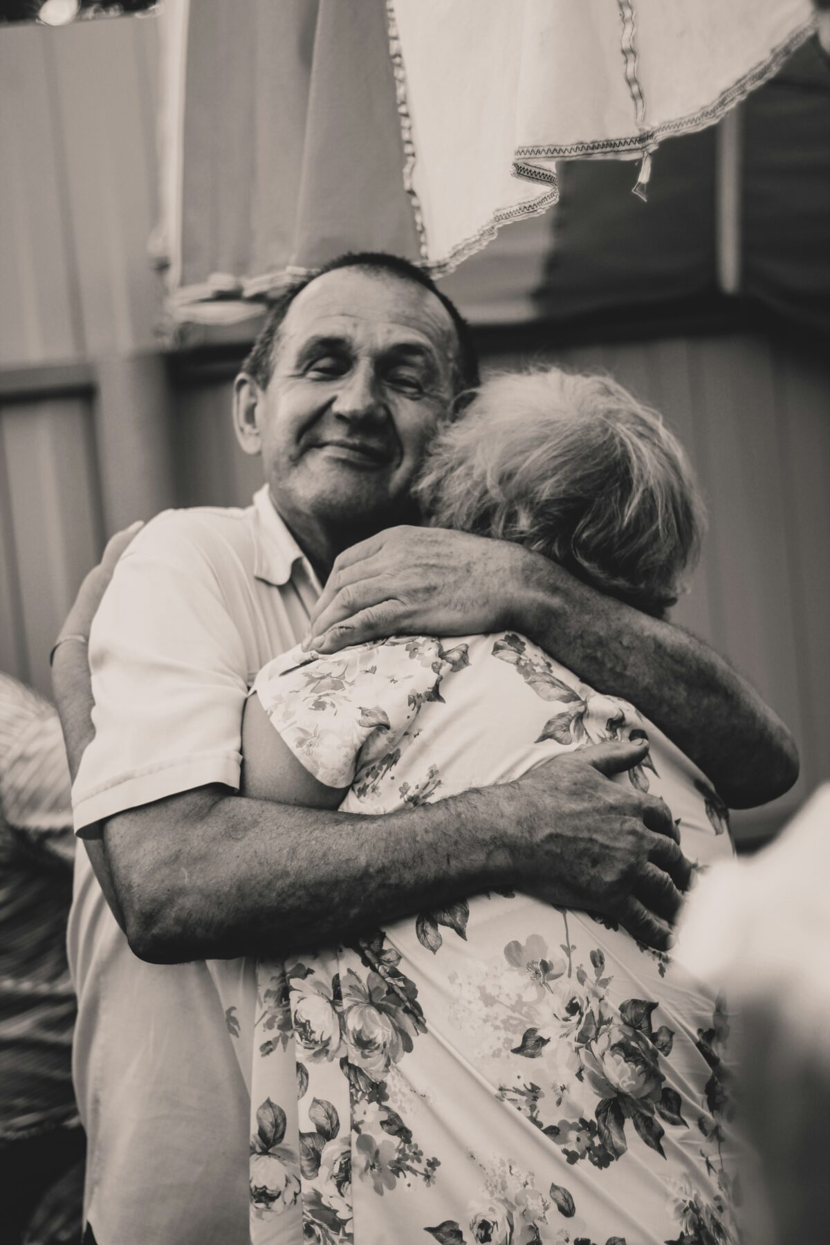 A black and white photo of two people hugging. The man is facing towards the photographer, his eyes are closed and he looks content