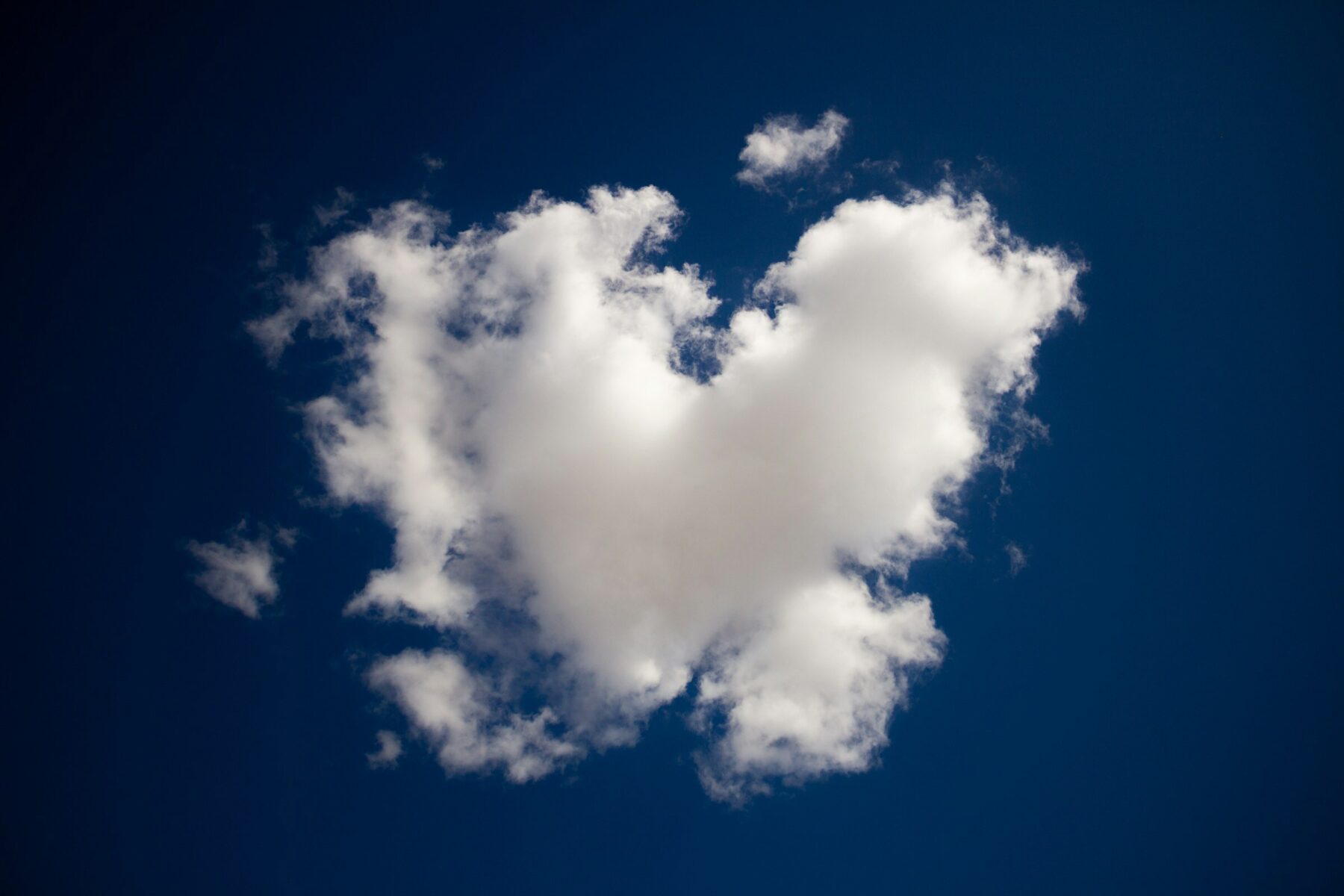 A close up of a deep blue sky with a fluffy white heart-shaped cloud