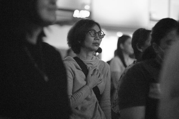 A place and white photo of a woman, in a crowded space, with her hand on her heart